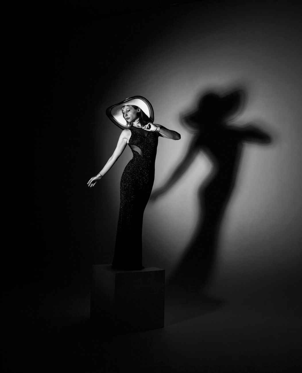 A model in a long dress and wide hat, her shadow thrown large on the studio wall