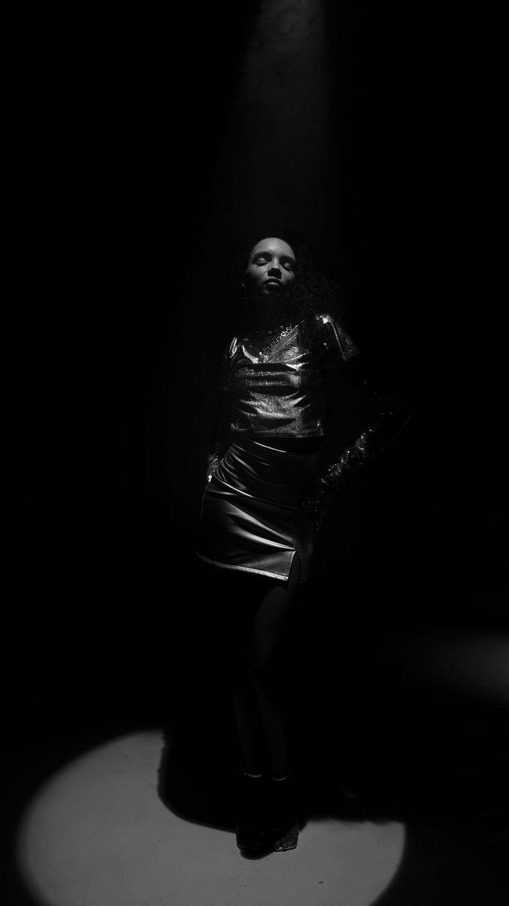 A model standing in a single shaft of light, surrounded by darkness