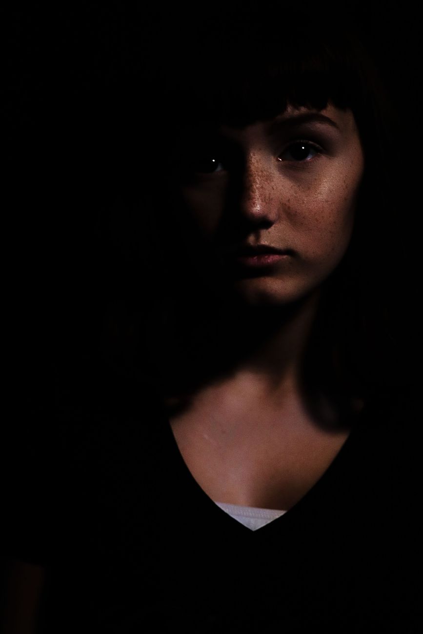 A woman's face half lit, emerging from deep shadow
